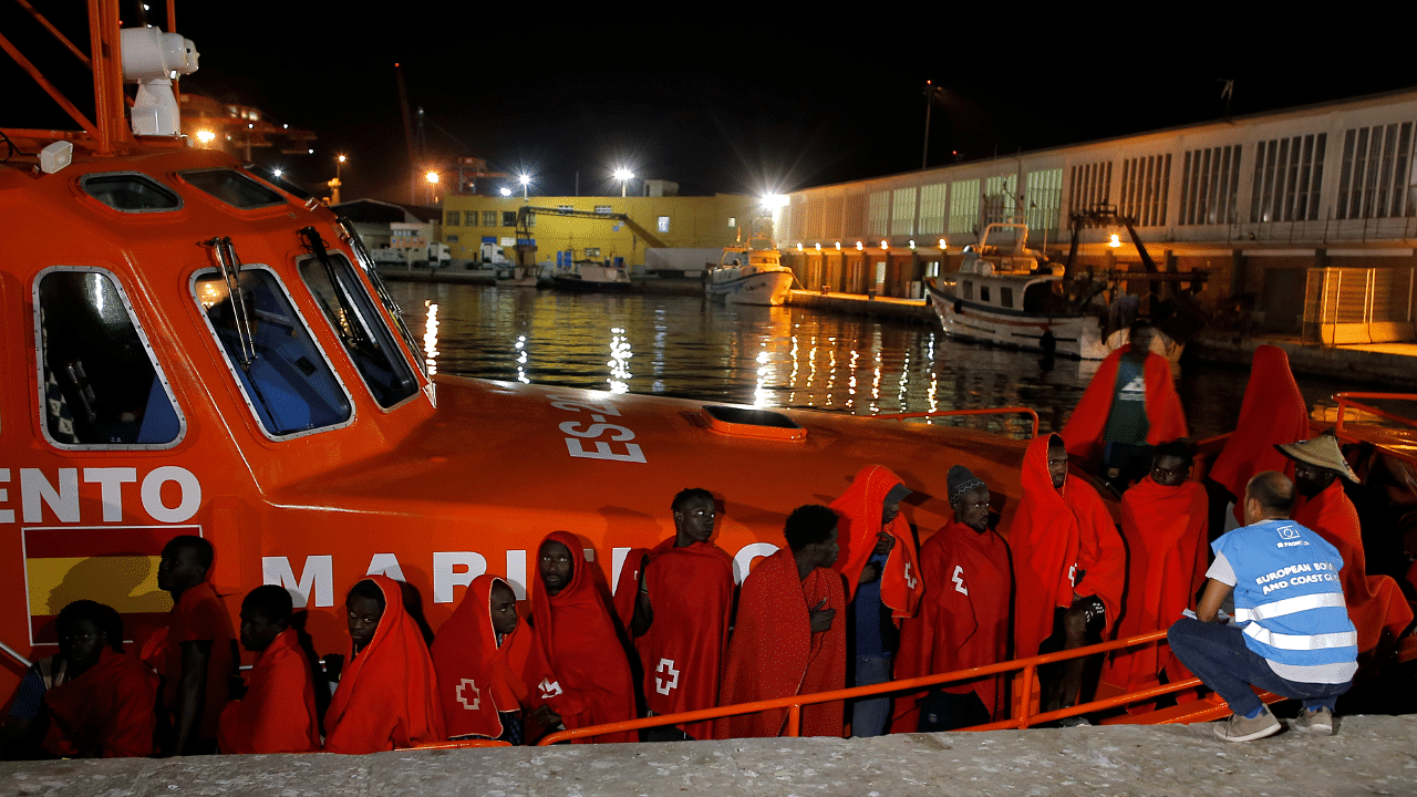 A member of Frontex talks to migrants as they wait to disembark from a rescue boat at the port of Malaga. Credits: Reuters Photo