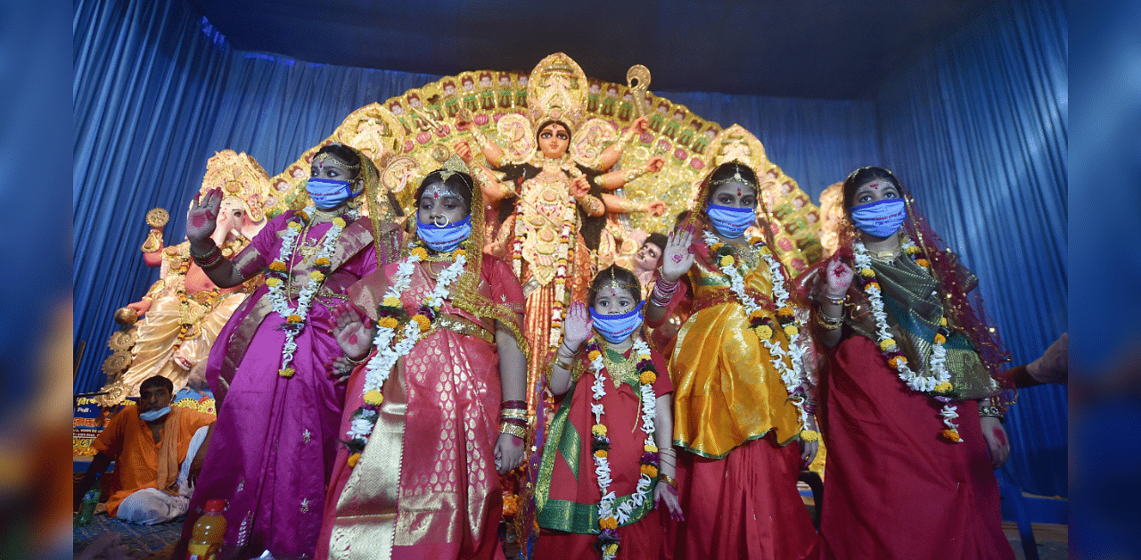 'Kumaris' (virgin girls) bless devotees from a safe distance while being worshipped as an incarnation of Goddess Durga at a community puja pandal, during Durga Puja festival. Credits: PTI Photo
