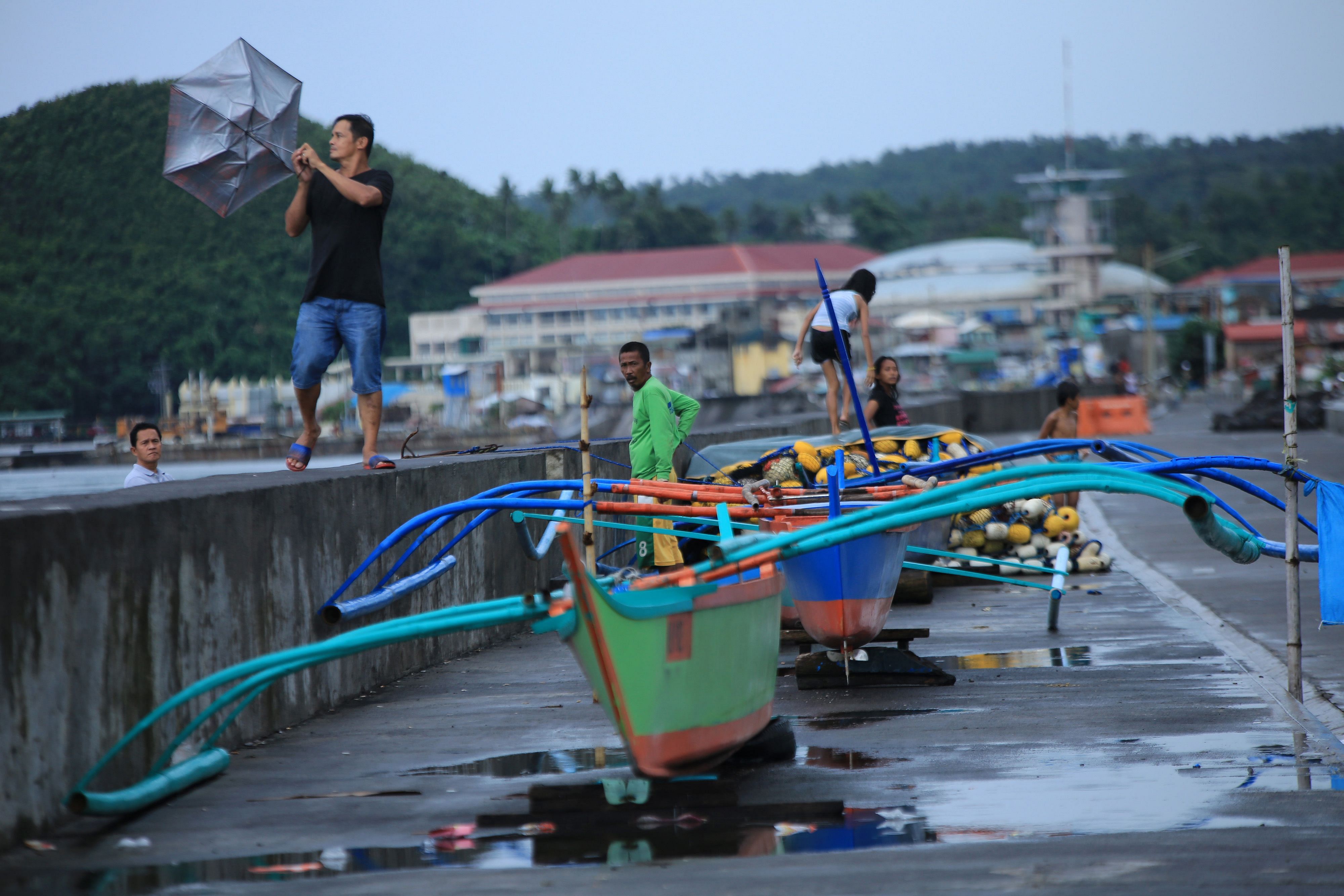 A resident holds onto his umbrella in strong wind as others stand by their wooden boats along the coastal area of Legaspi City, Albay province south of Manila on october 25, 2020, ahead of tropical storm Molave's expected landfall. Credit: AFP