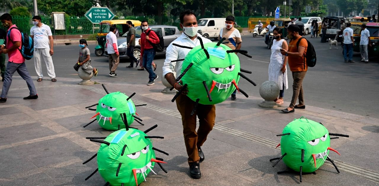 An officer from the district magistrate office holds a Covid-19 coronavirus-themed mascot in a market area during an awareness campaign against coronavirus and rising air pollution levels in New Delhi. Credit: AFP Photo