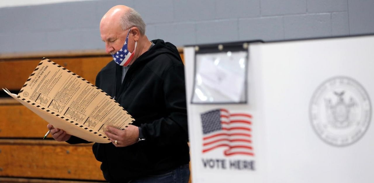A man wearing an American flag face mask checks a ballot at a polling station located in the Monsignor John D. Burke Memorial Gym at the Church of the Holy Child in Staten Island, during early voting in New York City. Credit: Reuters.