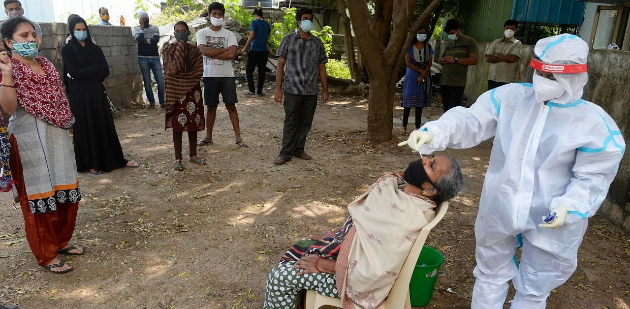 Residents watch as a health worker collects a swab sample from a woman to test for coronavirus at primary health centre on the outskirts of Hyderabad. Credit: AFP