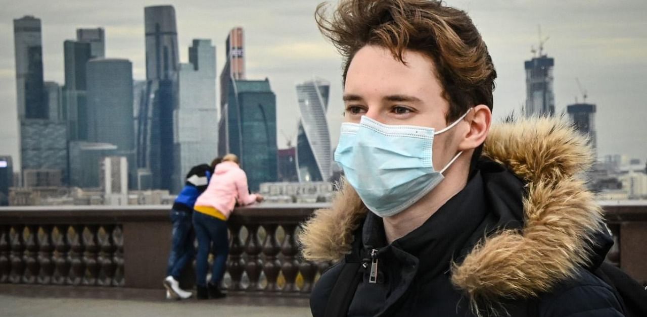 A man wearing a face mask walks at Vorobyovy Hills observation point with skyscrapers of the Moscow International Business Centre (Moskva City) seen in the background in Moscow. Credit: AFP.