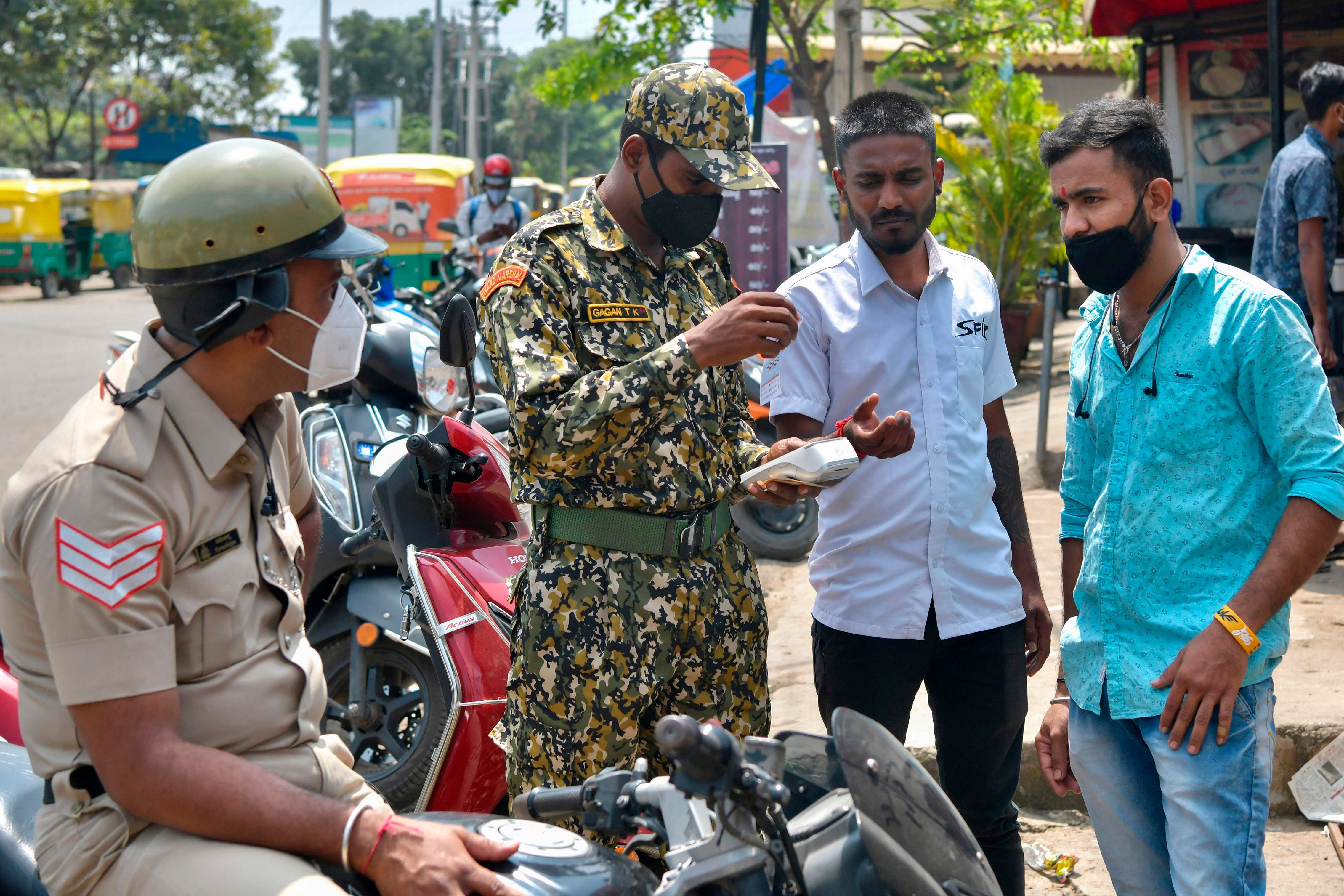 A police officer (L) along with a Bruhath Bengaluru Mahanagara Palike (BBMP) municipal marshal (2L) issue a fine to a man (2R) for not wearing a face mask amidst the Covid-19 pandemic in Bengaluru. Credit: AFP Photo