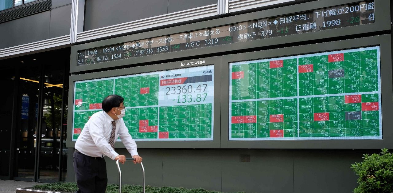 A man pushing a cart looks at an electronic quotation board displaying share prices of the Tokyo Stock Exchange in Tokyo. Credit: AFP Photo
