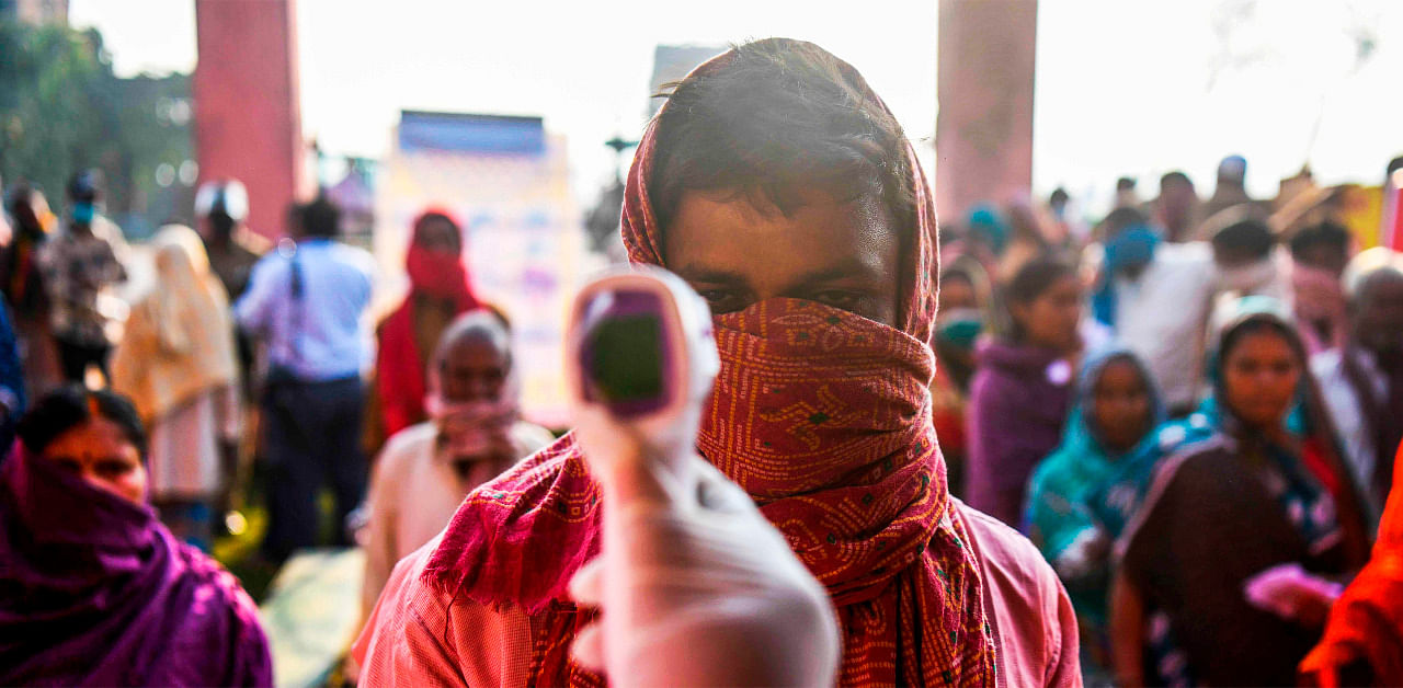 An electoral official checks body temperature of a voter as he waits to cast his ballot for Bihar state assembly elections at a polling station in Patna. Credit: AFP Photo