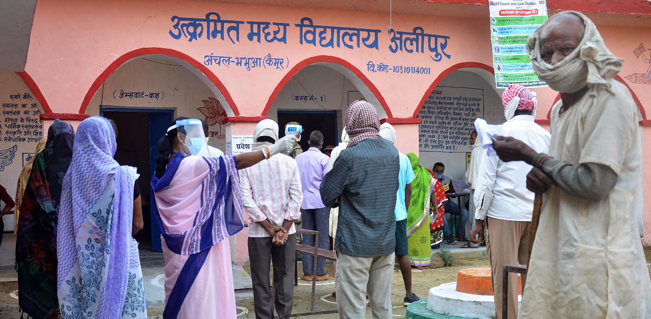 Voters undergo thermal screening at a polling booth as they stand in queues to cast their votes for the first phase of Bihar Assembly Election. Credit: PTI Photo