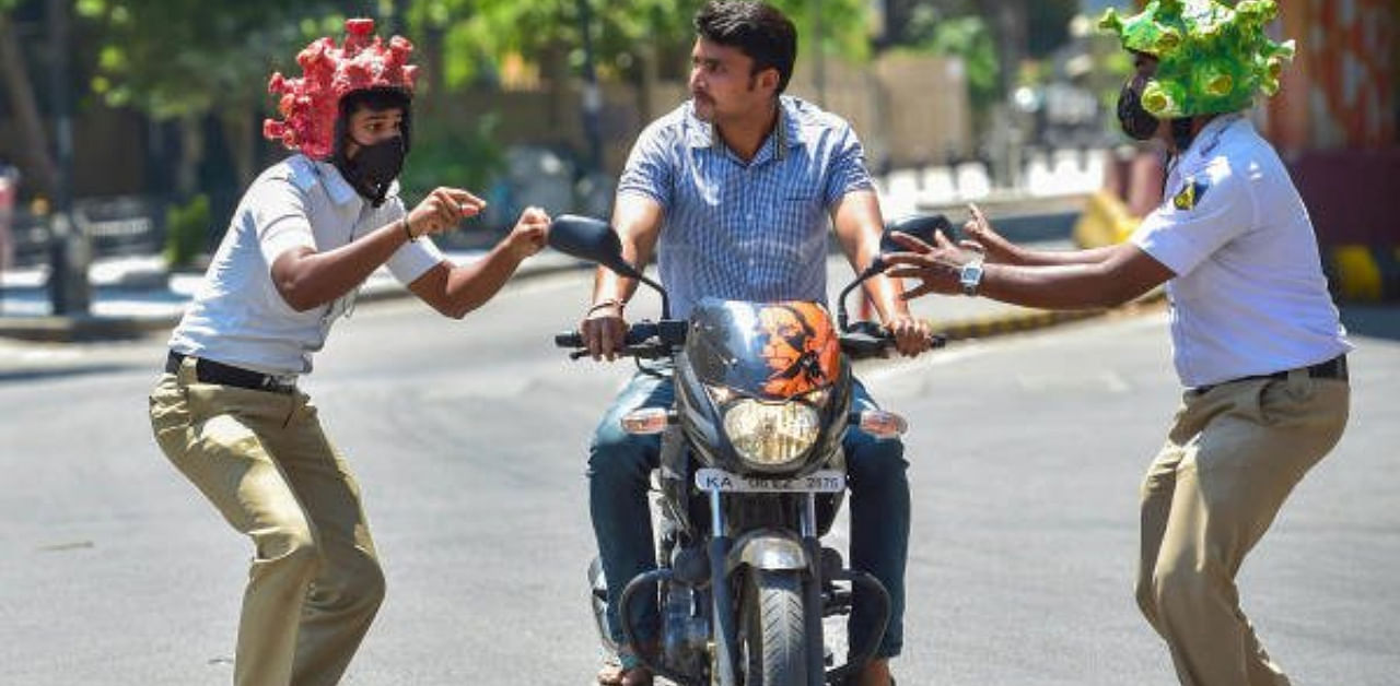 Two policeman wearing coronavirus-themed helmets charge another ríding a bike during an awareness programme amid the nationwide lockdown in the wake of novel coronavirus pandemic, in Bengaluru, Tuesday, Mar 31, 2020. Credit: PTI Photo