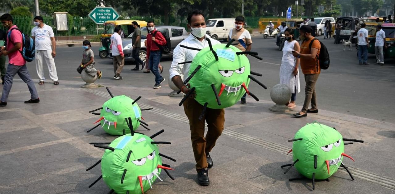An officer from the district magistrate office holds a Covid-19 coronavirus-themed mascot in a market area during an awareness campaign against coronavirus and rising air pollution levels in New Delhi on October 26, 2020. Credit: AFP Photo