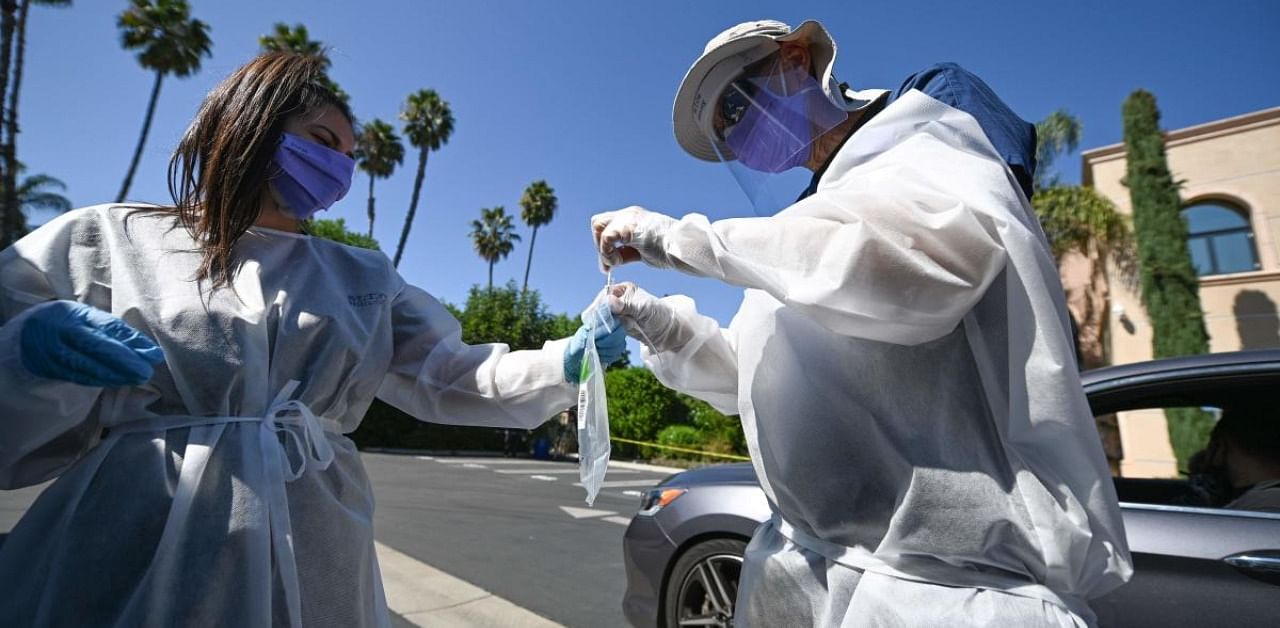 Healthcare workers collect a test sample at a drive-through coronaviurs (Covid-19) testing center. Credit: AFP