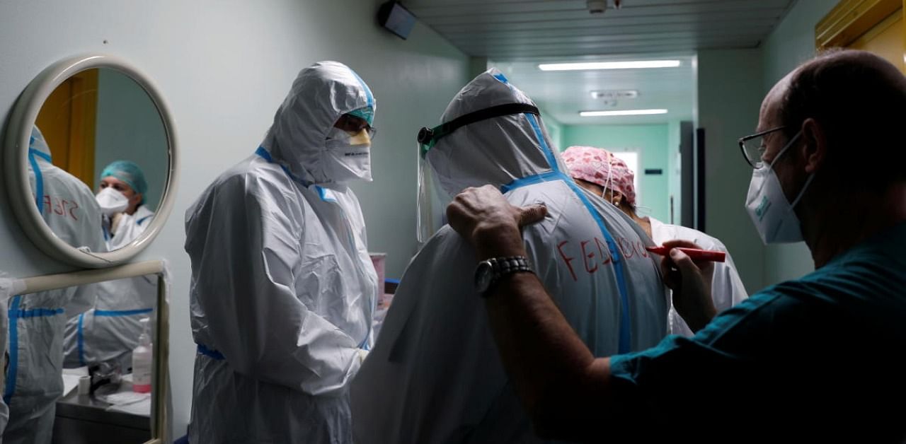 A medical worker helps a colleague to write his name on a personal protective equipment before going in an intensive care unit for the coronavirus disease. Credit: Reuters