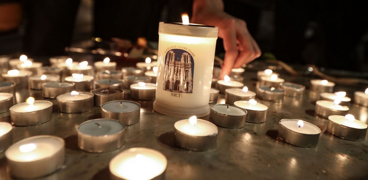 People lights candle outside the Notre-Dame de l'Assomption Basilica in Nice on October 29, 2020 in tribute to the three victims of a knife attacker, cutting the throat of at least one woman, inside the church of the French Riviera city. Credit: AFP Photo