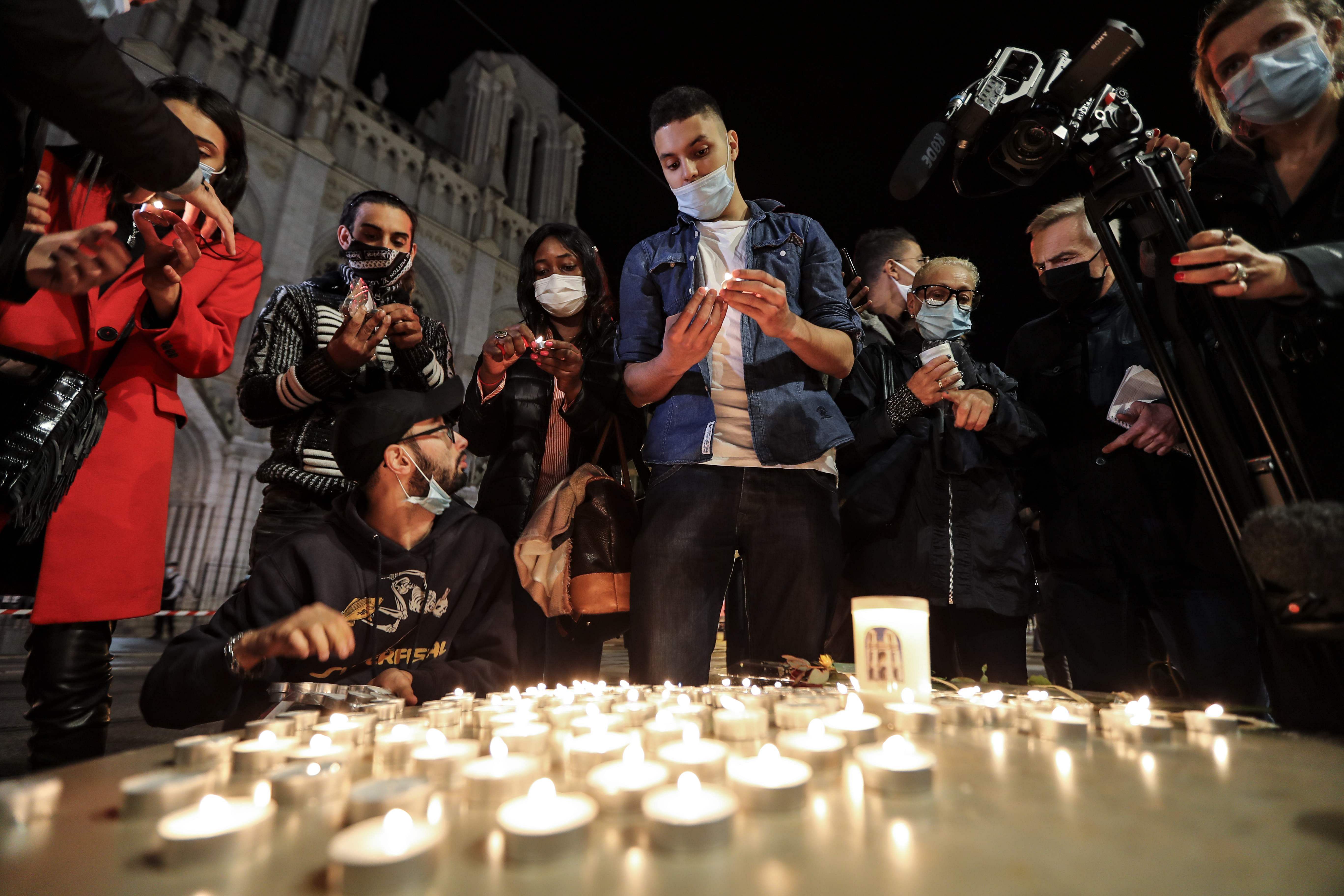People lights candle outside the Notre-Dame de l'Assomption Basilica in Nice on October 29, 2020 in tribute to the three victims of a knife attacker, cutting the throat of at least one woman, inside the church of the French Riviera city. Credit: AFP Photo