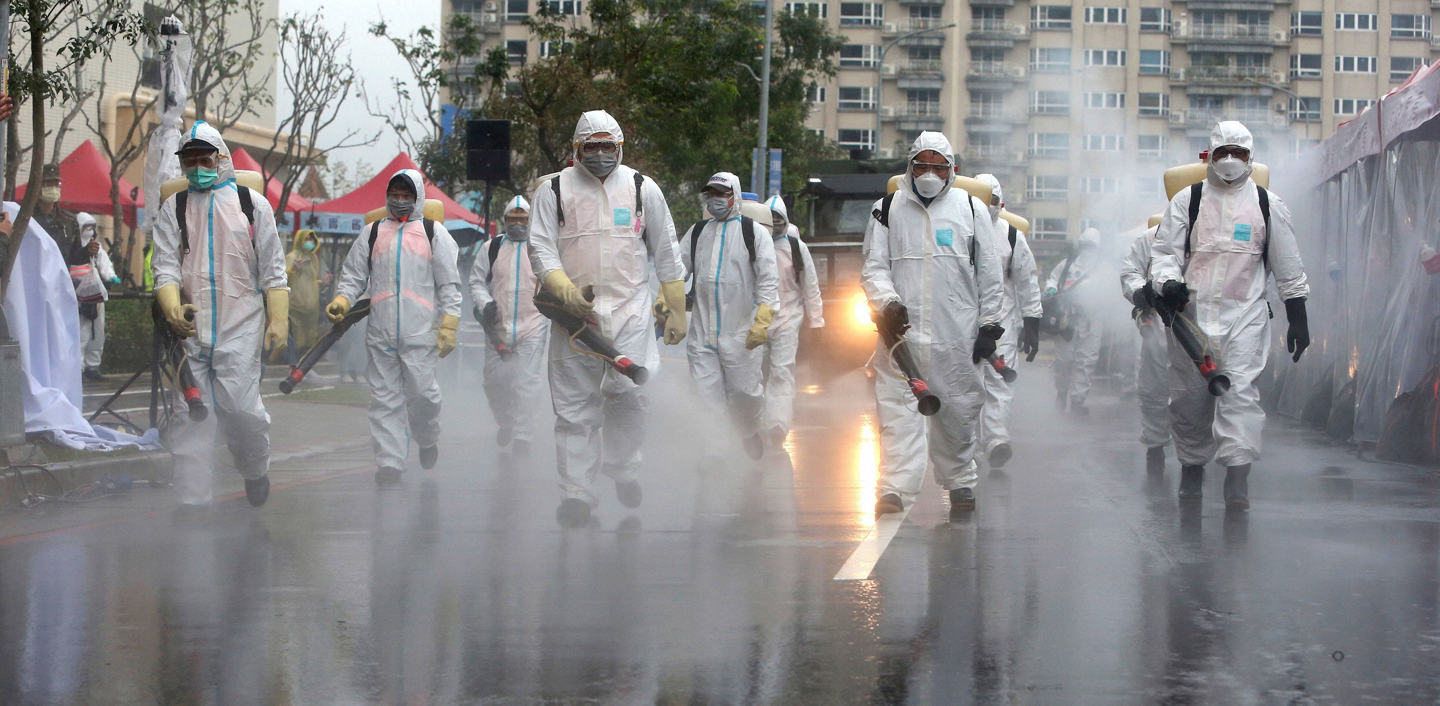 Taiwanese army soldiers wearing protective suits spray disinfectant over a road during a drill to prevent community cluster infection, in New Taipei City, Taiwan. Credit: AP