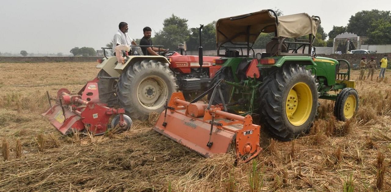 Tractors being used to level paddy stubble in a farm field after sprinkling of a bio-decomposer solution, at village Hiranki, North Delhi district. Credit: PTI
