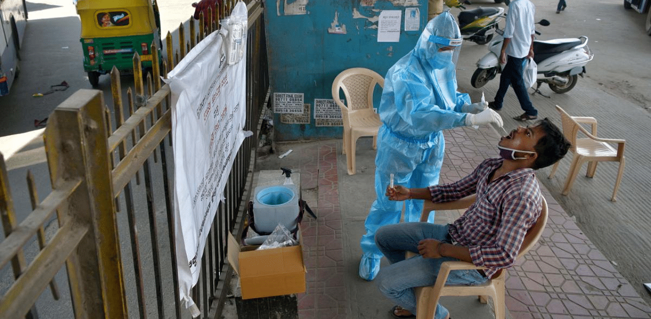 A health worker conducts swab test on a man at a mobile Covid-19 coronavirus testing clinic at a bus stand in Bangalore. Credit: AFP Photo