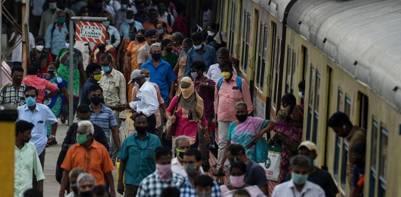 Commuters wearing facemasks to prevent the spread of the Covid-19 coronavirus walk along a platform at a train station in Chennai. Credit: AFP