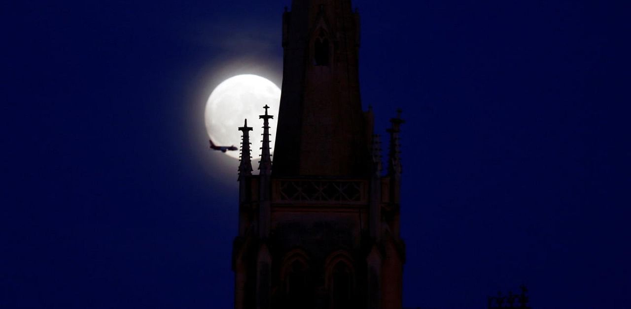 A plane flies in front of the full moon as it rises behind the steeple of the Chapel of Our Lady at the Santa Maria Addolorata Cemetery, before Halloween in Paola, Malta. Credit: Reuters