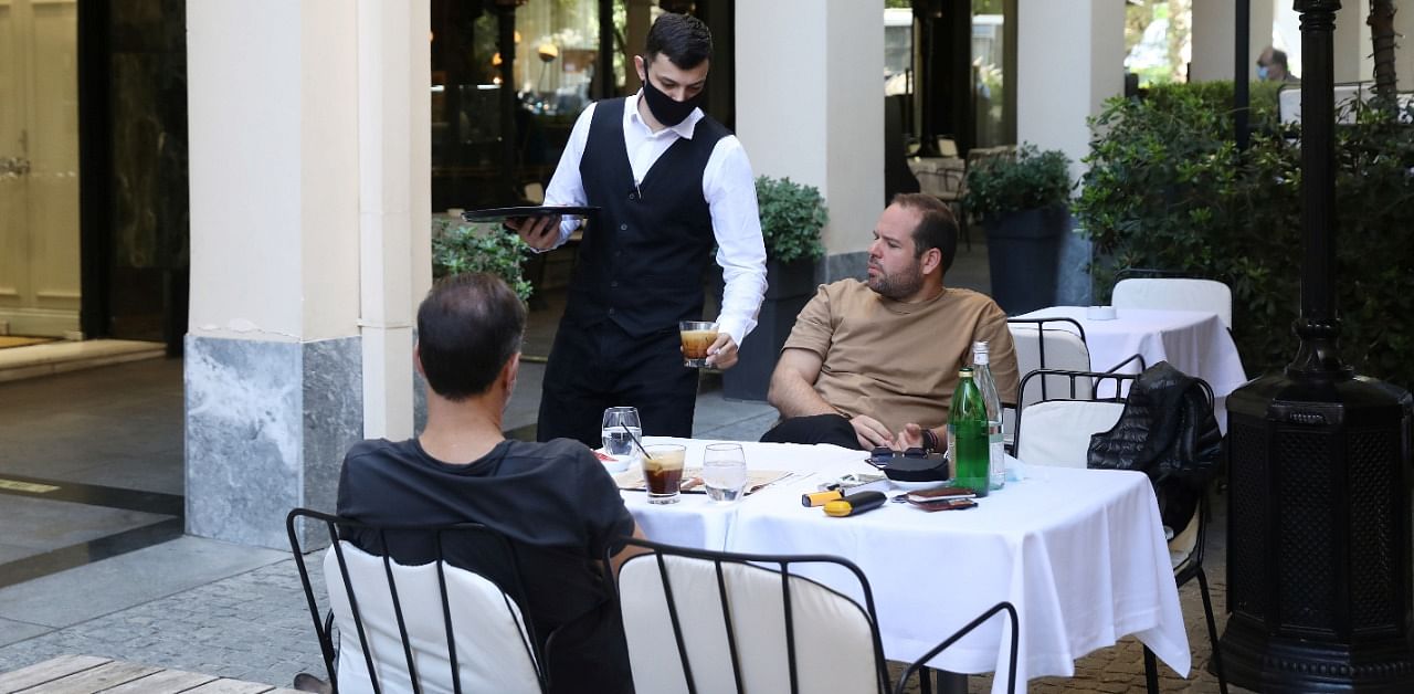 A waiter wearing a protective face mask serves customers at a coffee shop, amid the spread of the coronavirus disease. Credit: Reuters Photo