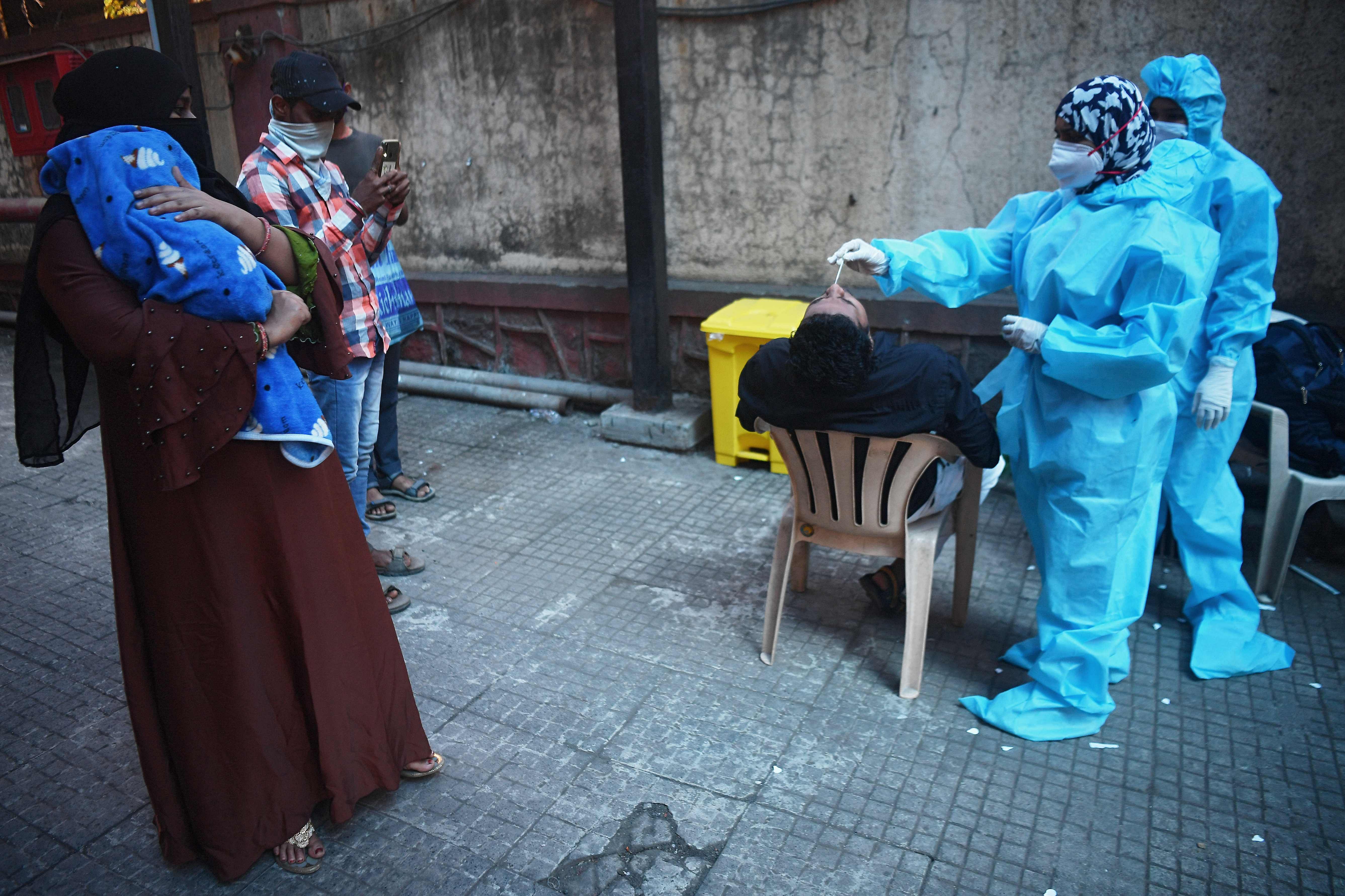  health worker collects a swab sample from a man as residents watch at a Covid-19 coronavirus screening. Credits: AFP Photo