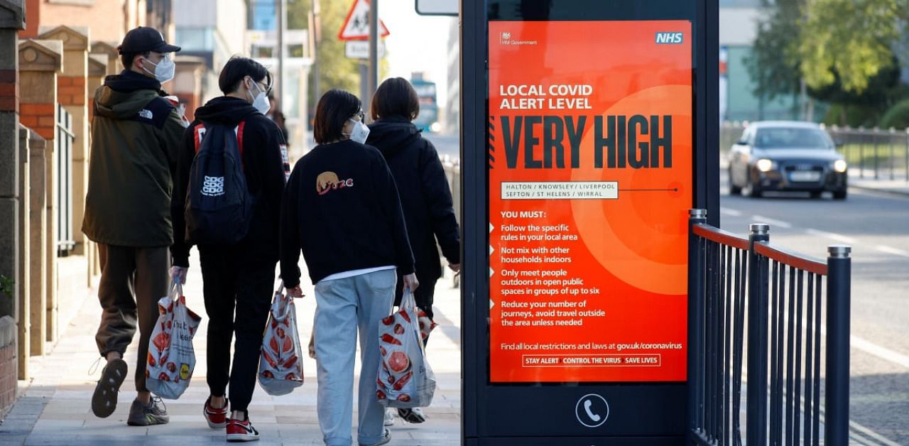 People wearing protective masks walk past a covid warning sign as the spread of the coronavirus disease continues in Liverpool. Credit: Reuters.