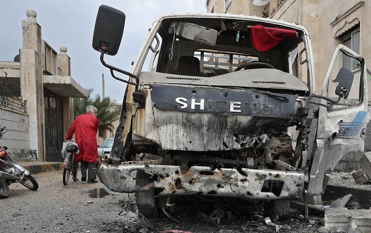 A Syrian man pushes his bicycle past a damaged vehicle following heavy shelling by Syrian government forces on the industrial area in the rebel-held northwestern Syrian city of Idlib. Credit: AFP