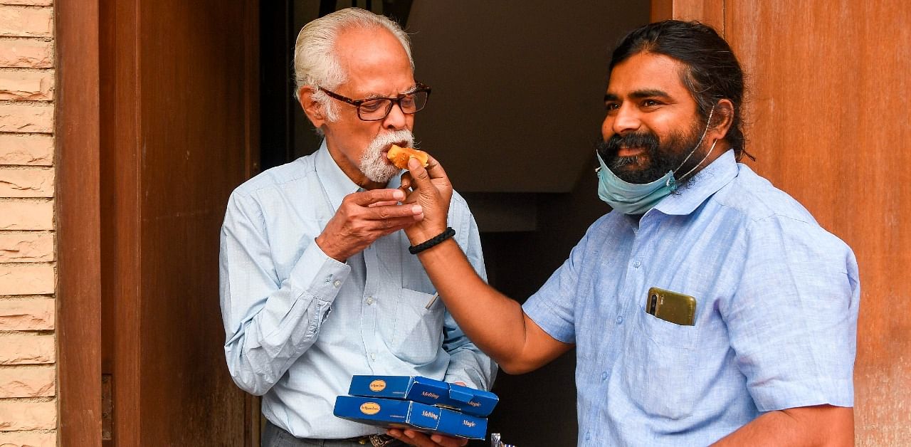 A man (R) from the native village of US Democratic Vice President-Elect Kamala Harris' uncle, Balachandran Gopalan (L), offers him sweets for Kamala Harris victory, at his home in New Delhi. Credit: AFP Photo