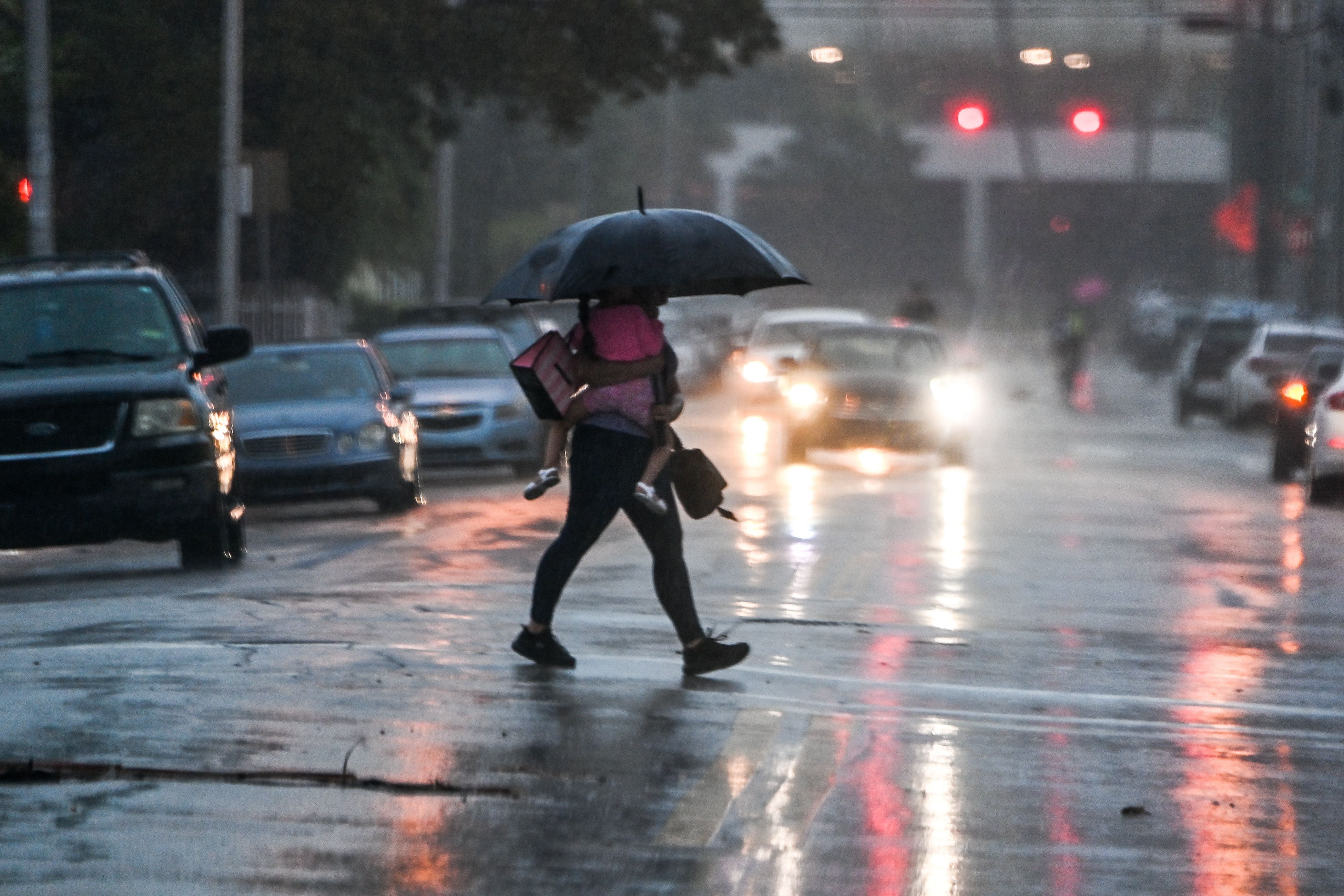 A man holds her daughter as he crosses the road during a heavy rain and wind as tropical storm Eta approaches south of Florida, in Miami, Florida on November 8, 2020. - Tropical storm Eta brought strong winds and torrential rain to Cuba on Sunday after having cut a destructive and deadly path through parts of Central America and southern Mexico. The storm crossed over Cuba's northern coast and was expected to head toward Florida while strengthening, with the US National Hurricane Center saying it was "forecast to become a hurricane before it reaches the Florida Keys tonight." Credit: AFP Photo