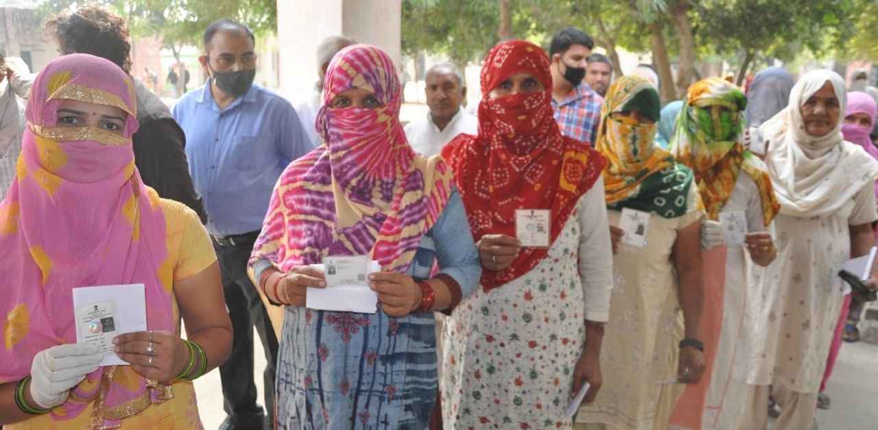 Voters show their ID cards as they stand in a queue to cast their votes for the state by-polls, amid the coronavirus pandemic, at Baroda. Credit: PTI