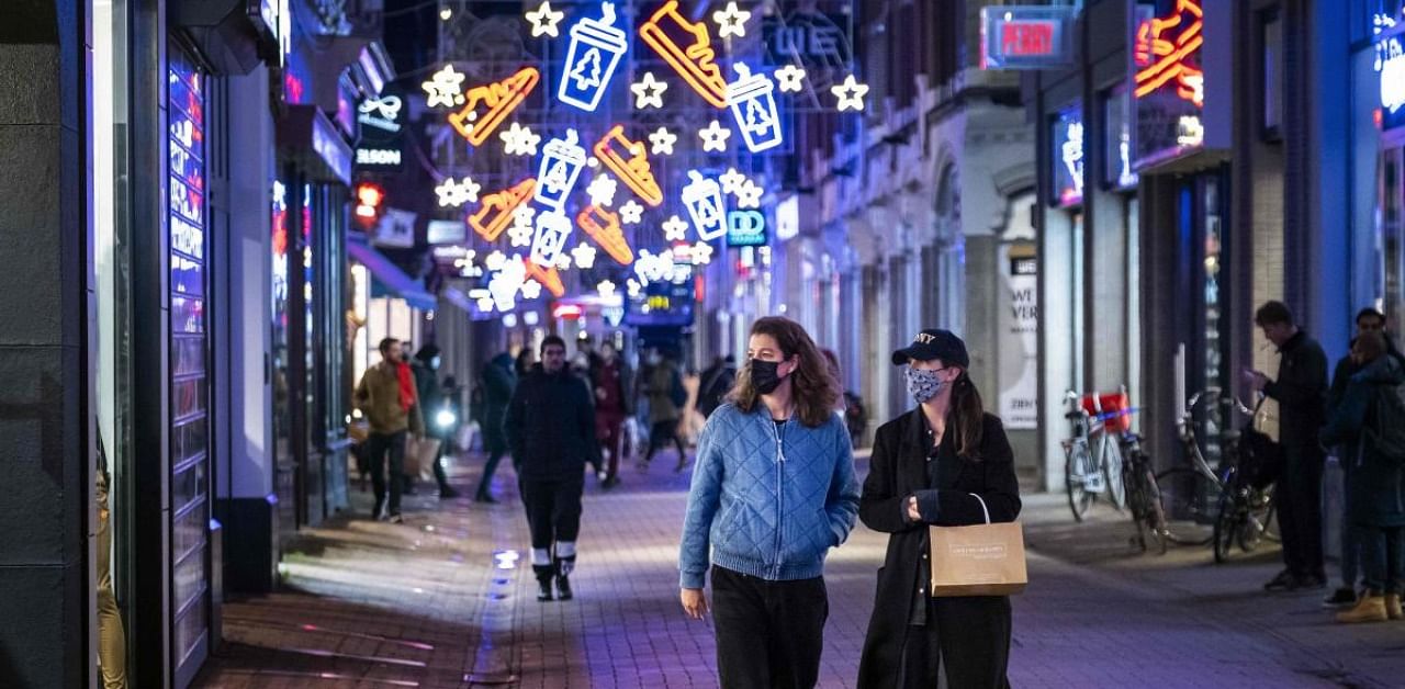 Pedestrians walk in a street under Christmas decorations in the city centre of Amsterdam. Credit: AFP