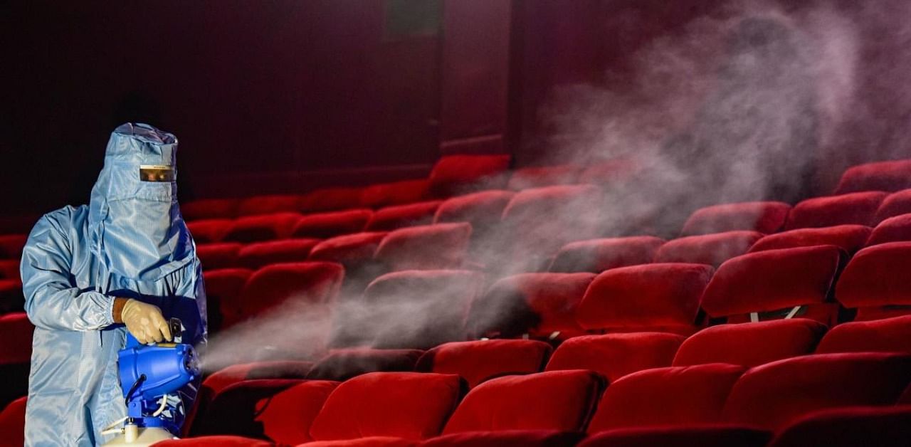 A worker wearing PPE kit sanitises a cinema hall, as mutilplexes prepare to re-open from October 15 after seven months of closure due to coronavirus lockdown, in New Delhi. Credit: PTI Photo