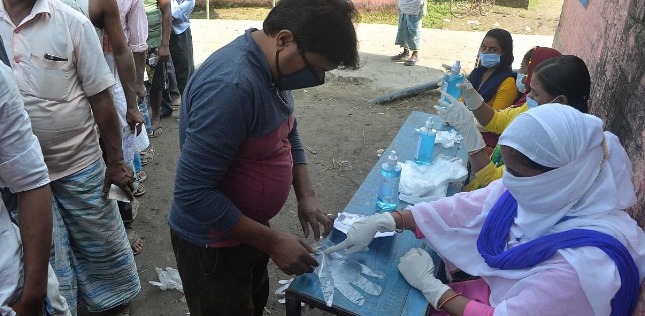 Polling offcials (R) provide gloves as voters queue up to cast their ballots during the last phase of Bihar state Assembly elections at a polling station in Thakurganj. Credit: AFP.