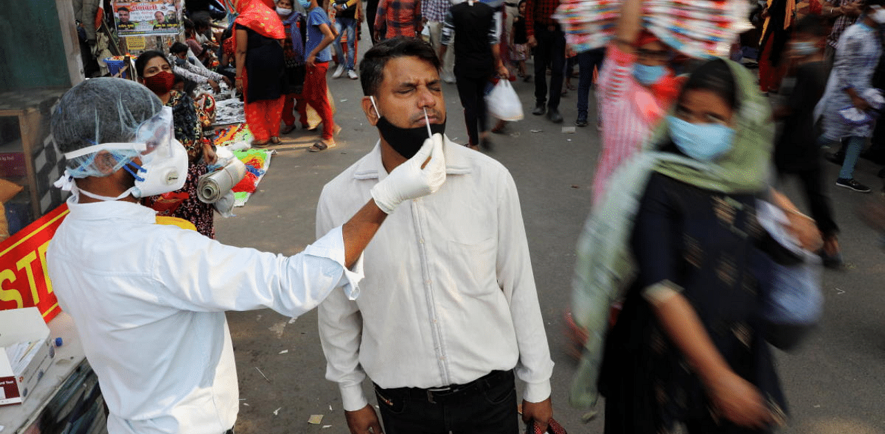 A healthcare worker collects a swab sample from a man amidst the spread of the coronavirus disease, at a market, in the old quarters of Delhi, India. Credit: Reuters Photo