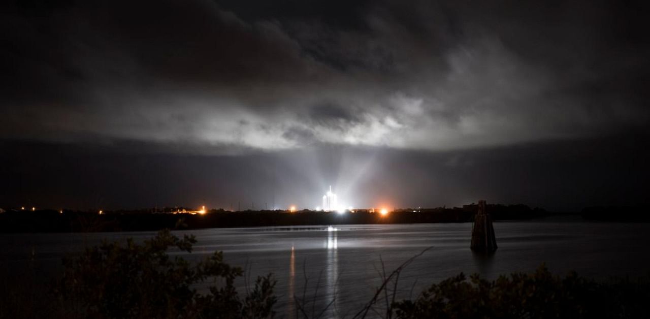 A SpaceX Falcon 9 rocket with the company's Crew Dragon spacecraft onboard illuminated by spotlights on the launch pad. Credit: AFP Photo