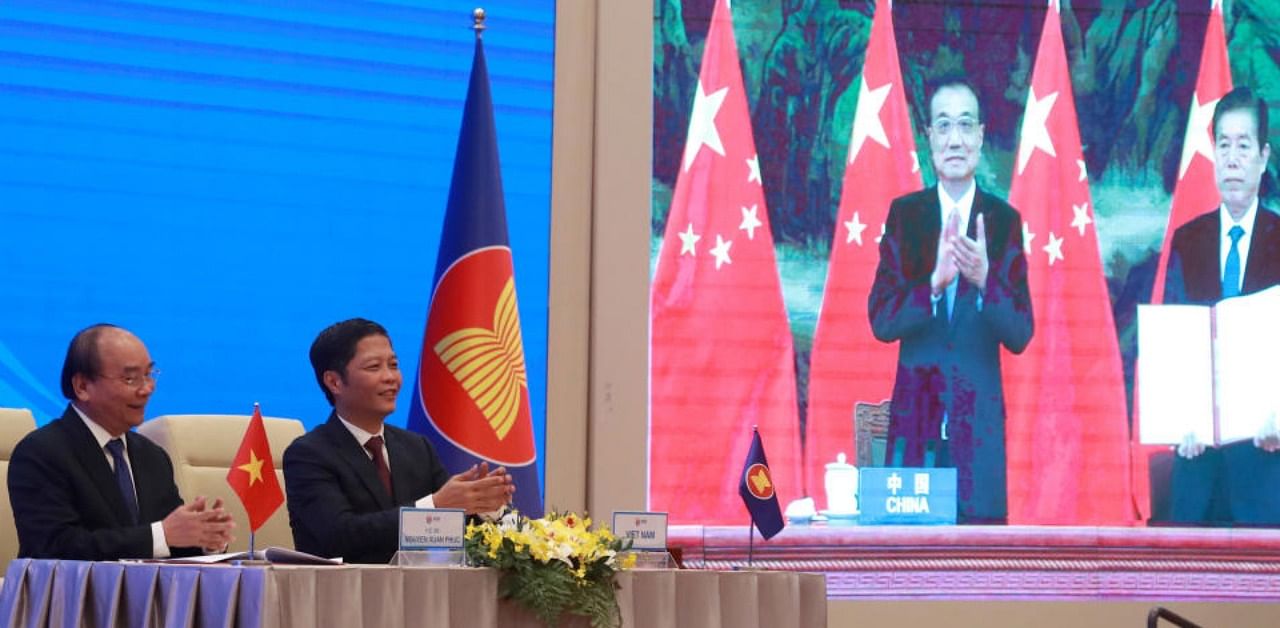 Vietnamese Prime Minister Nguyen Xuan Phuc, left, and Minister of Trade Tran Tuan Anh, right, applaud next to a screen showing Chinese Premier Li Keqiang and Minister of Commerce Zhong Shan holding up signed RCEP agreement, in Hanoi, Veitnam. China and 14 other countries have agreed to set up the world's largest trading bloc, encompassing nearly a third of all economic activity, in a deal many in Asia are hoping will help hasten a recovery from the shocks of the pandemic. Credit: AP
