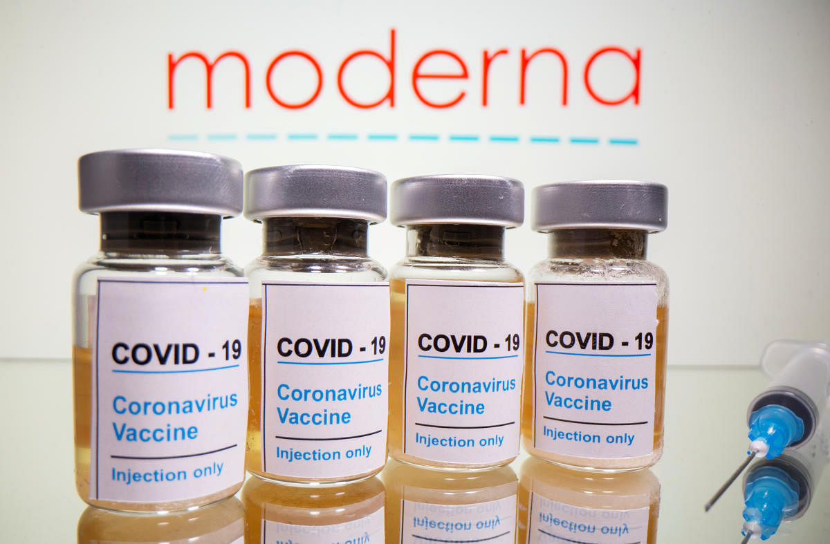 Vials with a sticker reading, "Covid-19 / Coronavirus vaccine / Injection only" and a medical syringe are seen in front of a displayed Moderna logo. Credit: Reuters