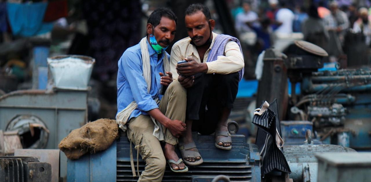 Men wearing protective face masks on their chins, amid the Covid-19 outbreak, watch a video on a mobile phone as they sit at a second-hand motor parts market in the old quarters of Delhi. Credit: Reuters.
