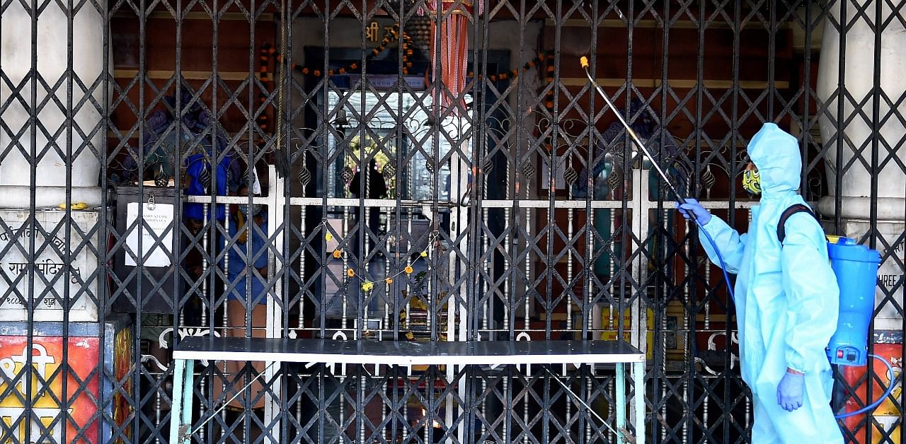 An employee, wearing a PPE kit, sanitizes the premises of a Hindu temple in Mumbai. Credit: PTI Photo