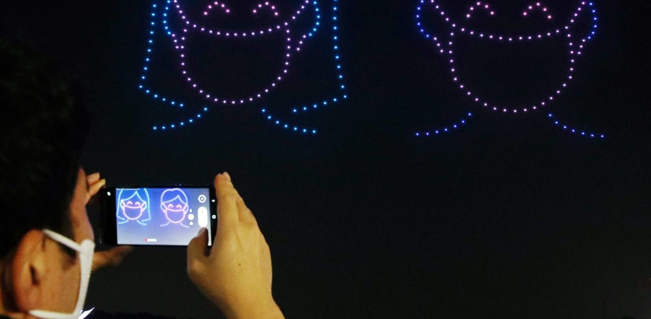 A spectator takes photos as 315 illuminated drones perform a routine to display messages and images of support for South Korea amid the coronavirus pandemic. Credit: AFP Photo