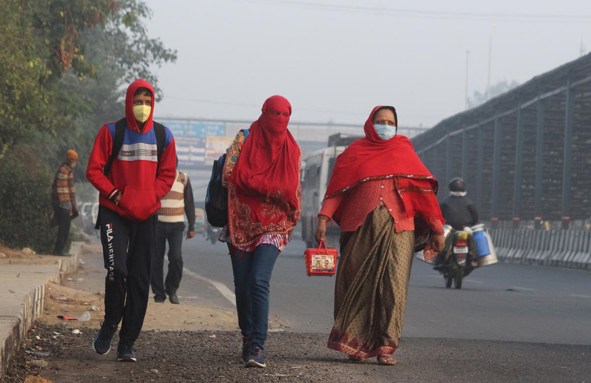 People wearing warm clothes walk along a road, in Gurugram. Credit: PTI