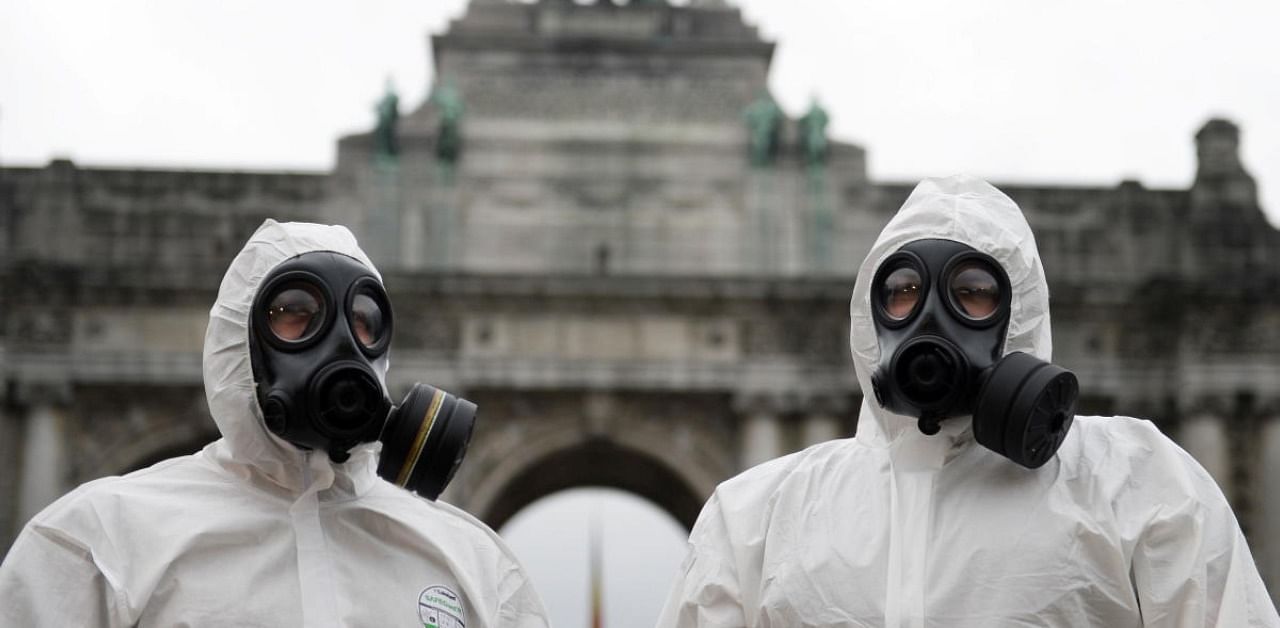 Belgian military personnel members wearing full protective suits stand in front of the Cinquantenaire arch during the disinfection of an ambulance amid the coronavirus disease outbreak. Credit: Reuters Photo