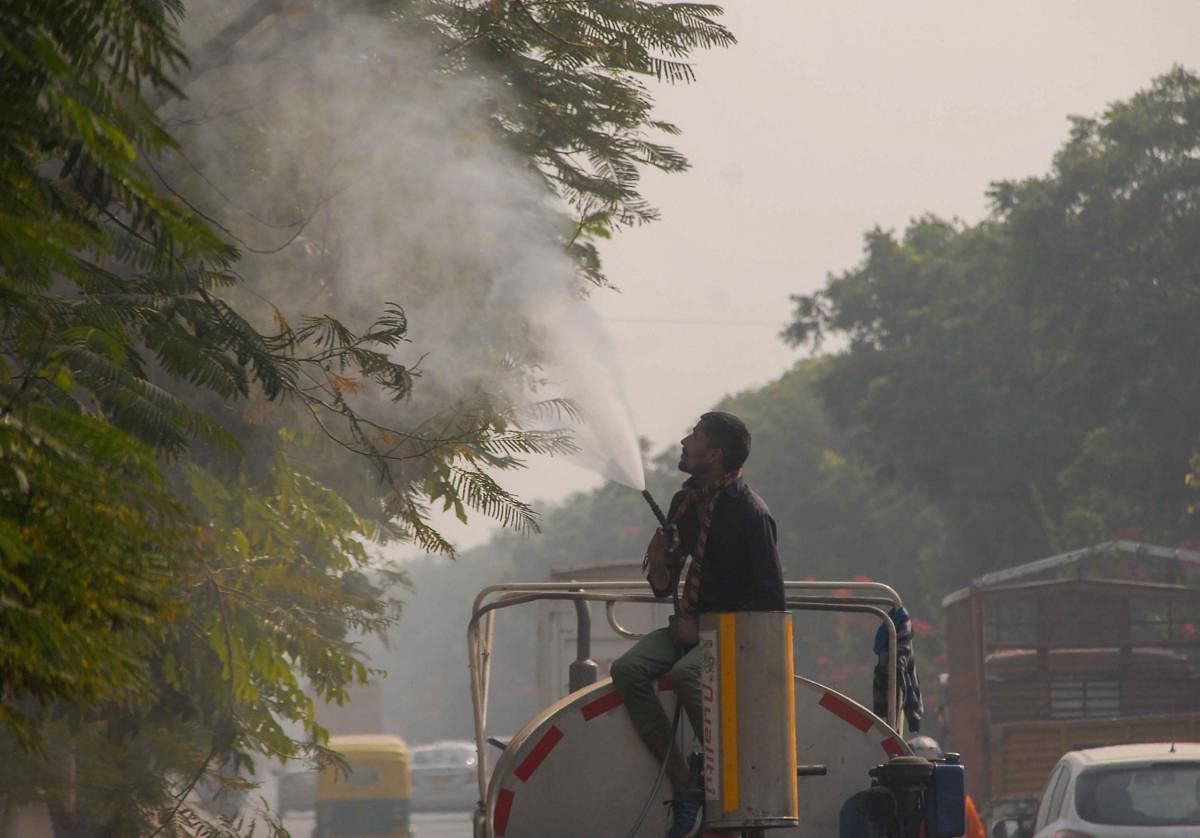 A worker sprays water on trees to curb dust pollution, in Noida. Credit: PTI