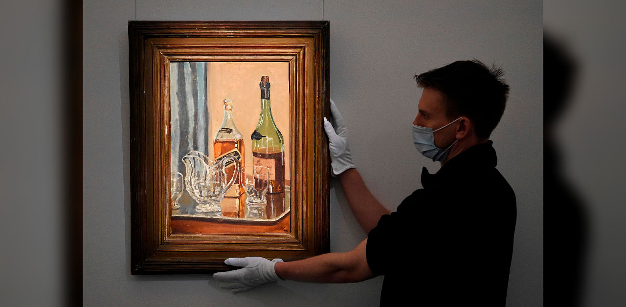   A member of staff poses with a painting by Britain's former prime minister Winston Churchill entitled "Jug with Bottles" at Sotheby's auction house in London on November 9, 2020. - A painting by Winston Churchill featuring the famously bibulous wartime leader's favourite brand of whisky is to go on sale at London's Sotheby's auction house, a spokeswoman said Monday. The oil painting of a bottle of Johnny Walker's Black label whisky and a bottle of brandy with a jug and glasses reflects Churchill's fondness for the blend, which he often drank first thing in the morning with soda water, the auction house said. Painted at Churchill's country house of Chartwell, the still life called "Jug with Bottles" is going on sale on November 10 and is expected to sell for up to £250,000. Credit: DANIEL LEAL-OLIVAS / AFP