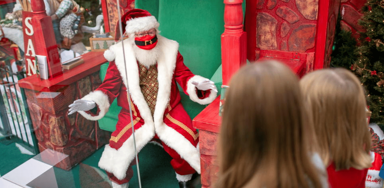 Santa Claus wears a face mask and sits behind a plexiglass divider due to the coronavirus disease (COVID-19) pandemic, as he greets sisters Charlotte, 11, and Savannah Smith, 8, at the Exton Square Mall in Exton, Pennsylvania, U.S. November 14, 2020. Credit: Reuters Photo