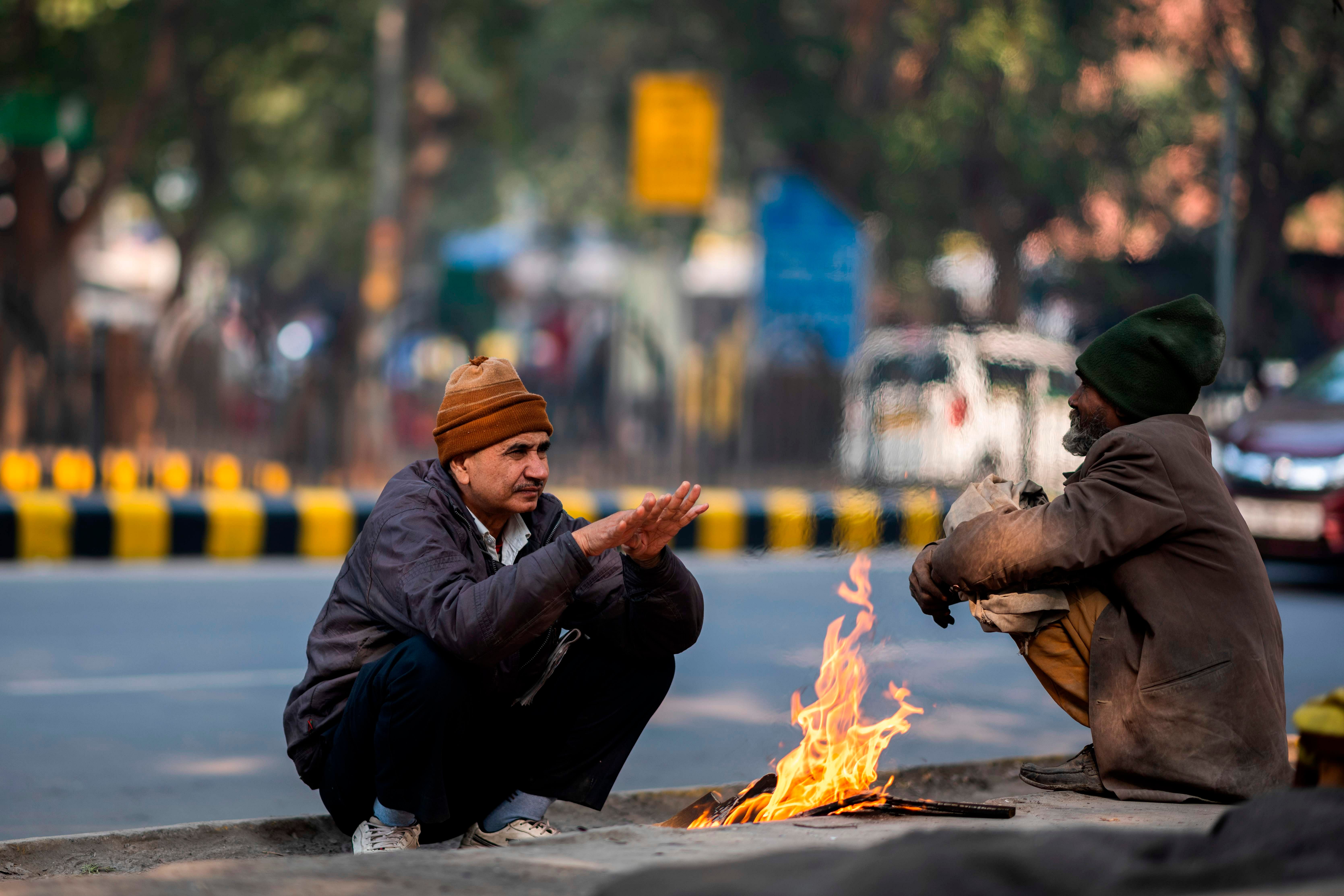 Two men sit in front of a small fire to warm themselves up on a cold morning in New Delhi. Credit: AFP Photo