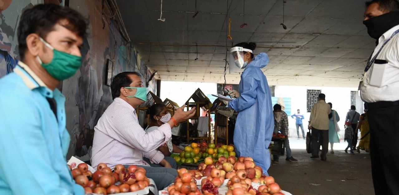 A health worker, wearing protective gear, speaks to a fruit vendor during a campaign to detect coronavirus spread outside Dadar market, in Mumbai. Credit: PTI Photo
