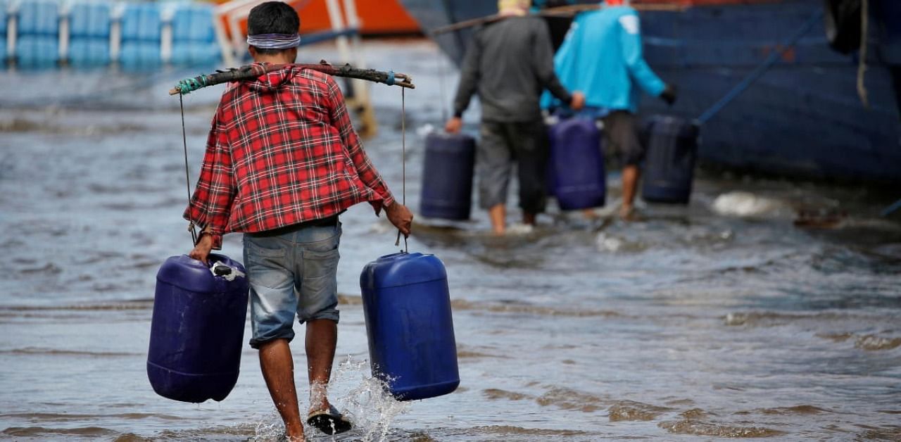 Workers carry jerrycans with clean water through floods at the Kali Adem port, which is impacted by high tides due to the rising sea level and land subsidence in Indonesia. Credit: Reuters Photo