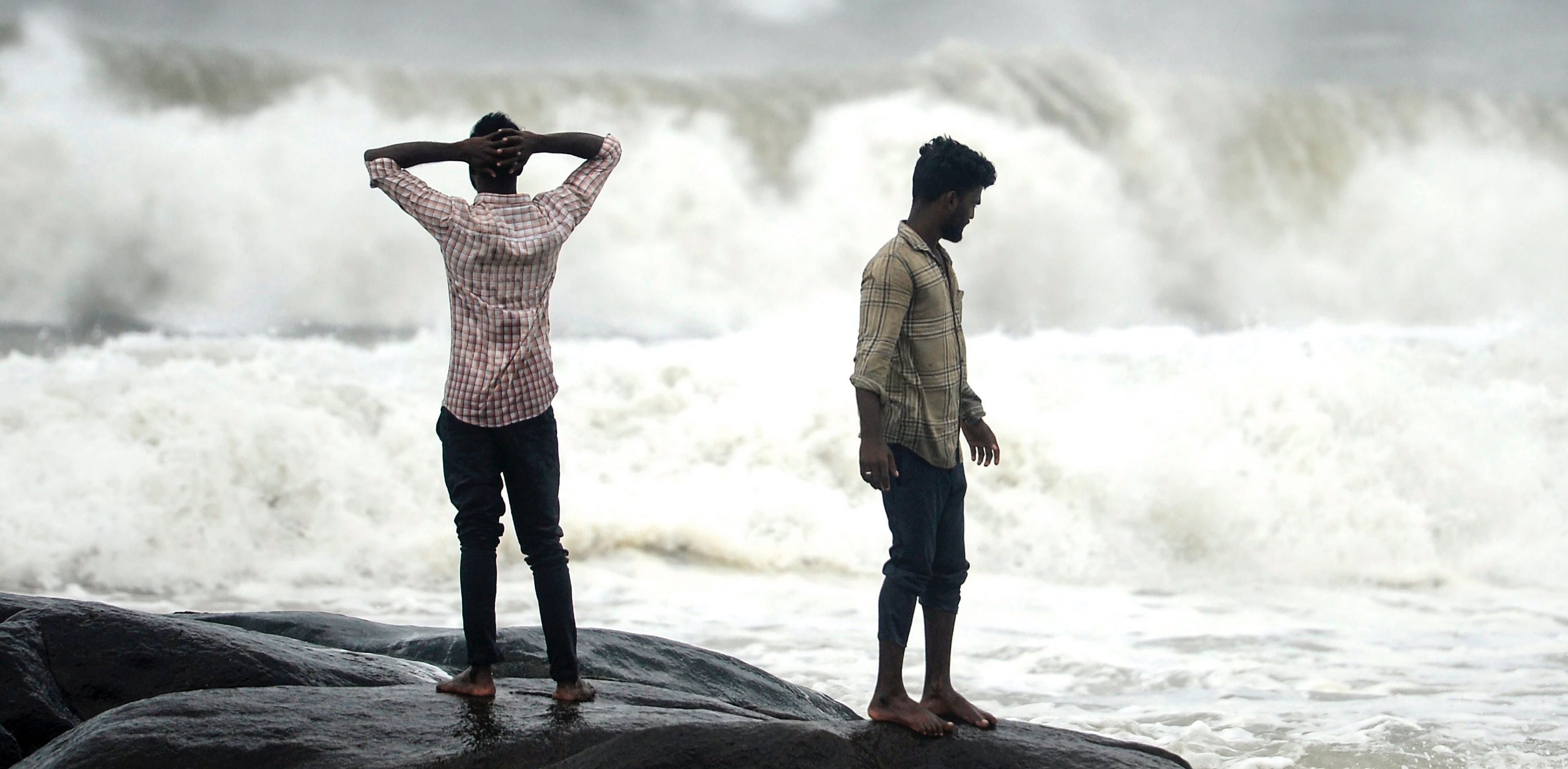People stand on a rock while waves lashes over at Kovalam beach as cyclone Nivar approaches the eastern Indian coast, in Chennai. Credit: AFP