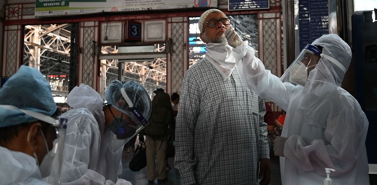 A health worker wearing protective suit takes a nasal swab of a passenger for a Covid-19 RT PCR and Rapid Antigen test after arriving from New Delhi. Credit: AFP Photo
