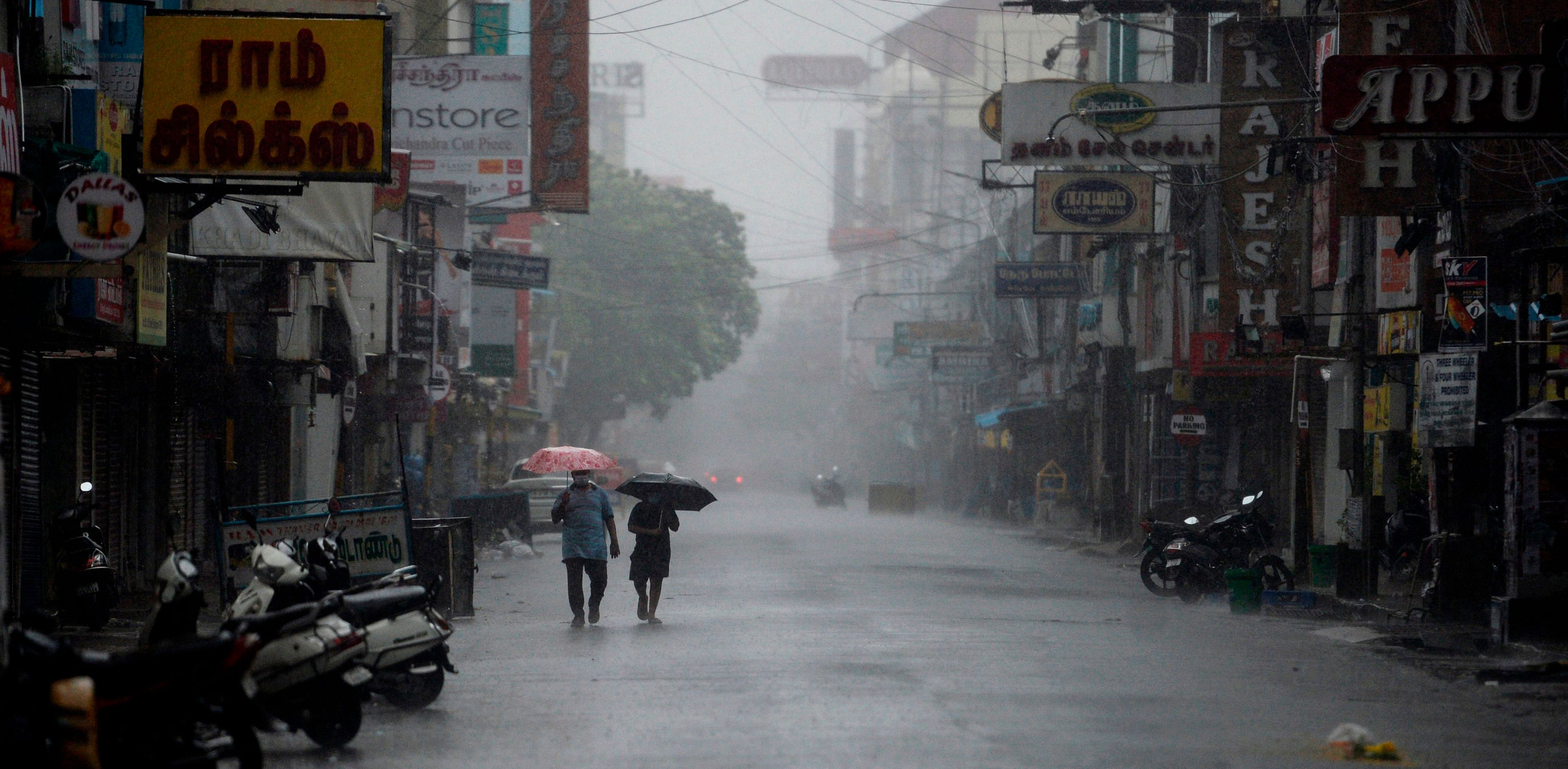 Residents shelter from heavy rain under umbrellas while walking along a deserted road as cyclone Nivar approaches. Credit: AFP